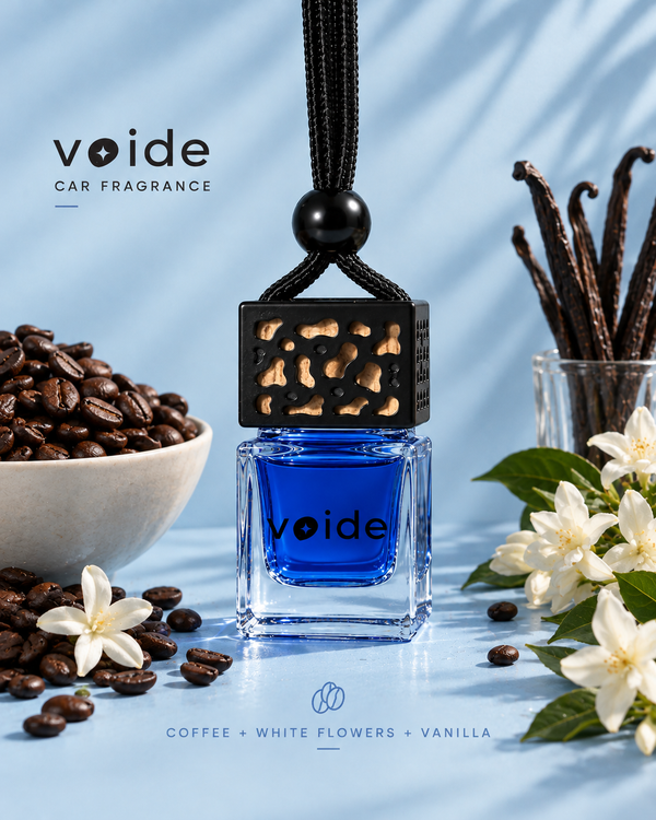 Descent car fragrance: blue coffee and vanilla oil in a glass bottle with a black cap, next to coffee beans, vanilla and white flowers