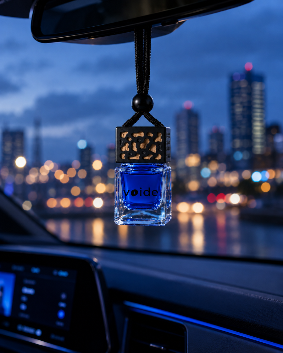 Descent car fragrance hanging from a rear-view mirror with city lights at night